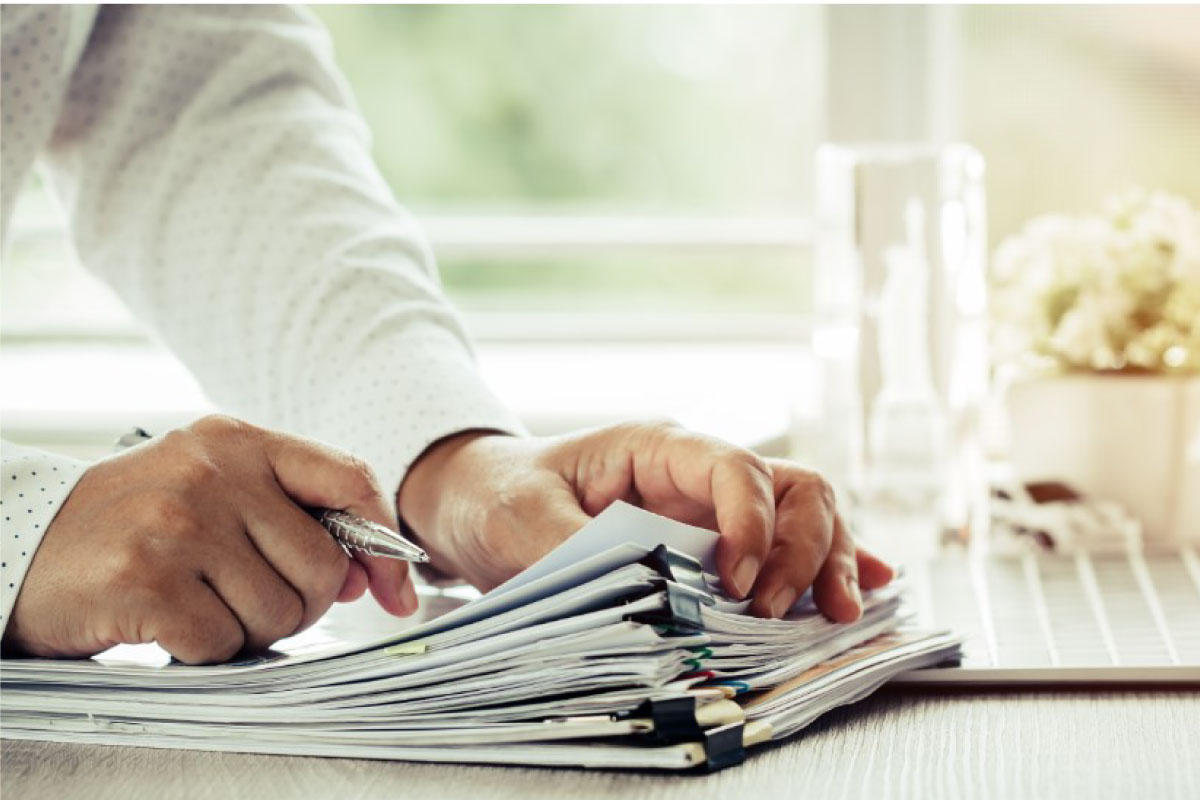 Persona con un boligrado en su mano y varias hojas de papel
