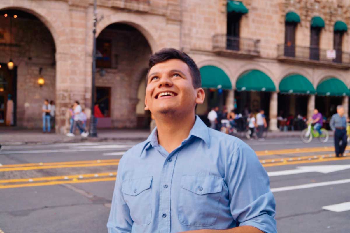 Hombre joven en la calle mirando alegremente hacia la punta de un edificio.