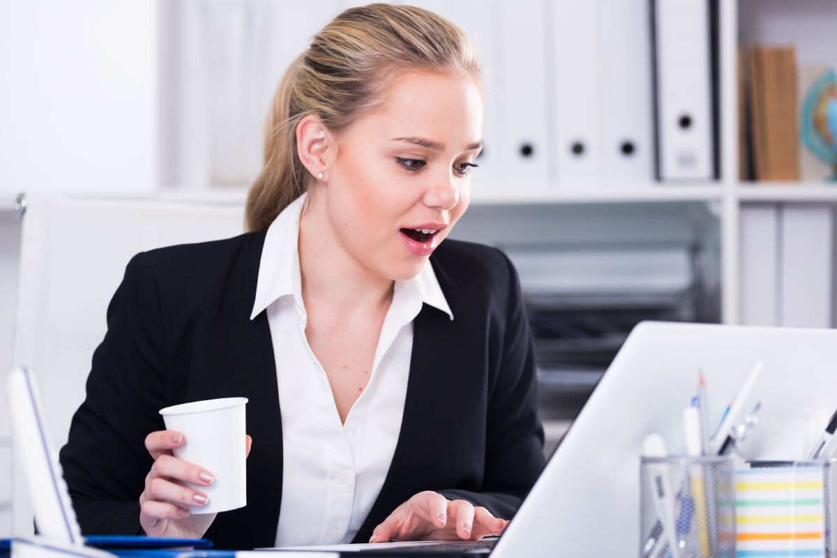 Mujer de negocios joven, trabajando en un computador portatil y con un vaso en su mano.