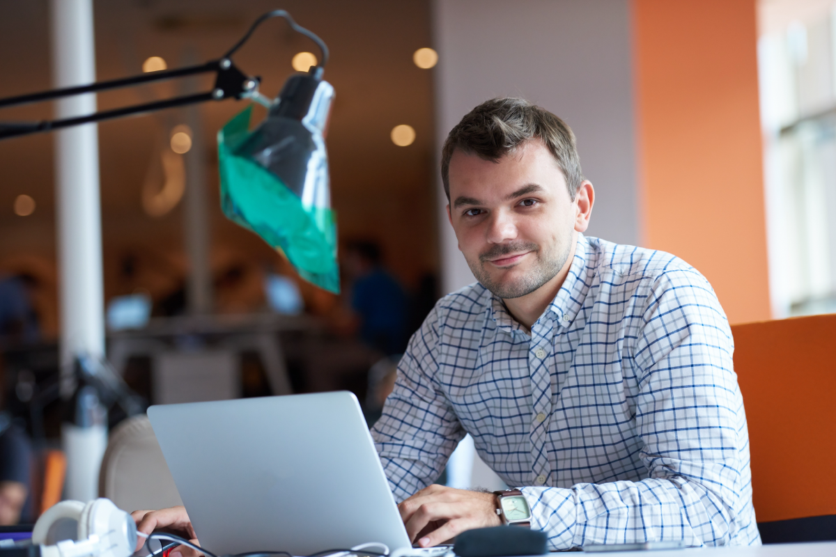Hombre joven, trabajando en un computador portatil, sonriendo y mirando a la cámara.
