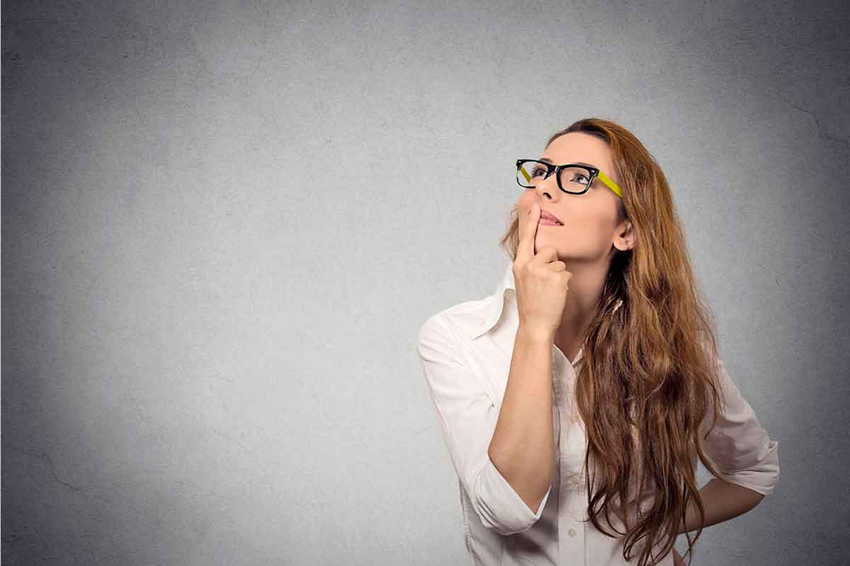 Mujer joven con un dedo sobre su boca, mirando hacia un lado y arriba, pensando.