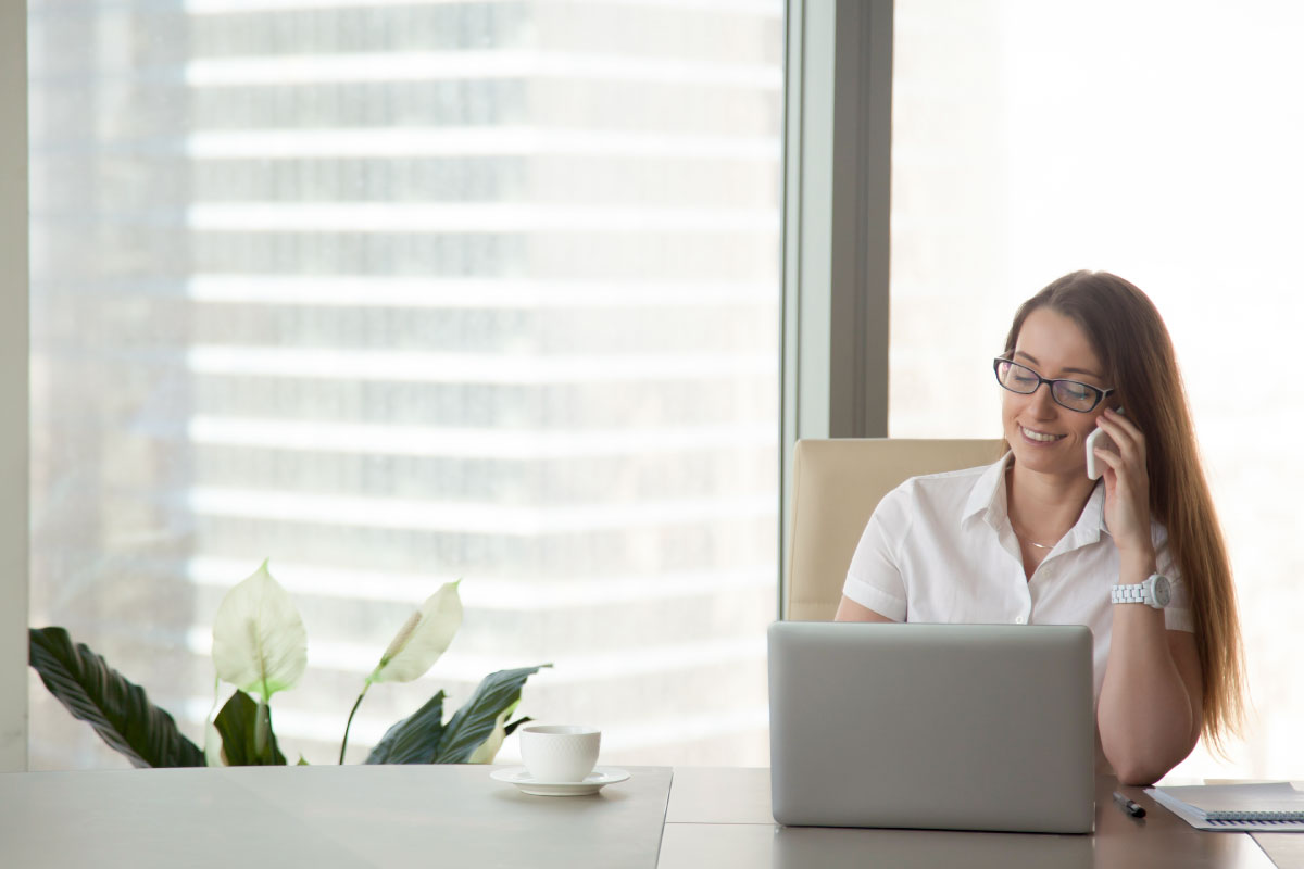 Mujer sentada al frente de un computador portatil hablando por teléfono.