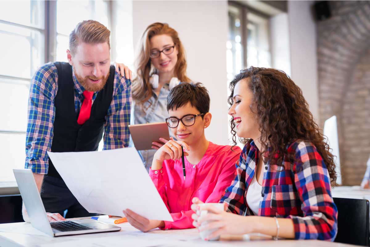 Mujer sosteniendo un papel en sus manos mientras tres de sus compañeros observan y analizan la misma información