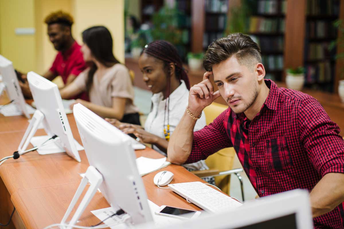Grupo de cuatro personas, cada una sentada al frente de un computador en una sala internet.