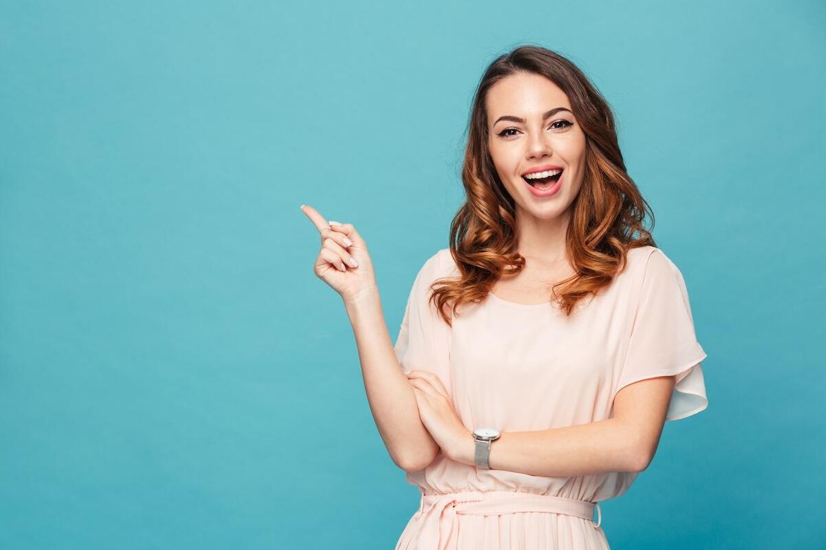 Mujer joven y sonriente al frente de una pared verde, señalado a su lado.