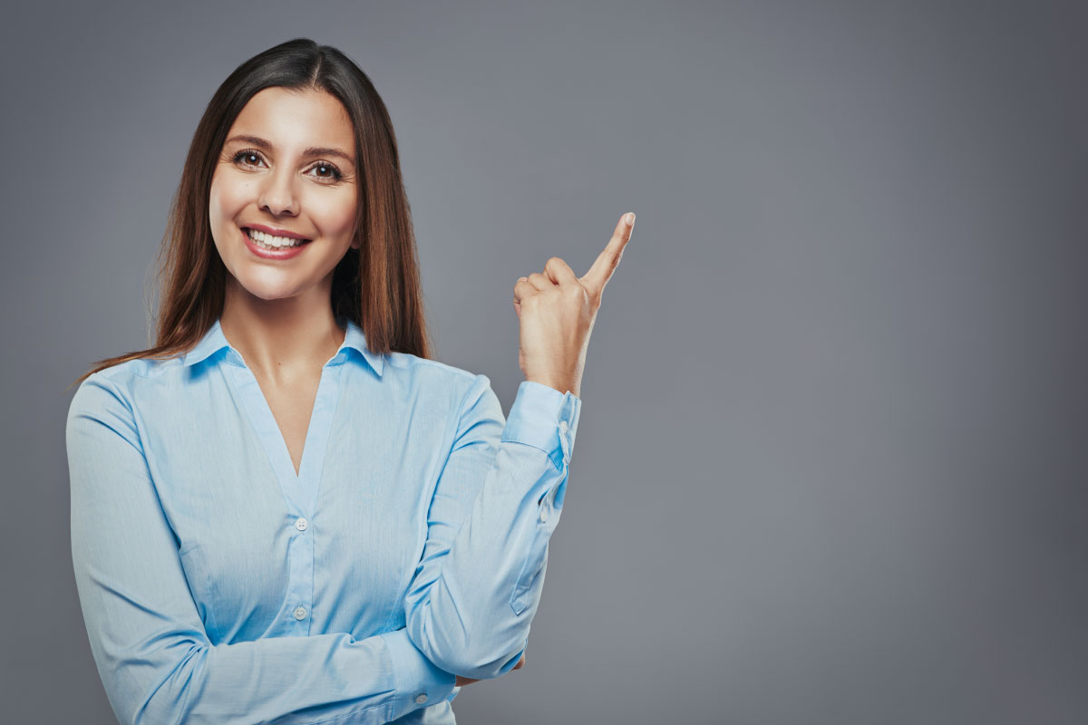 Mujer joven sonriendo y señalando con su dedo índice hacia arriba.