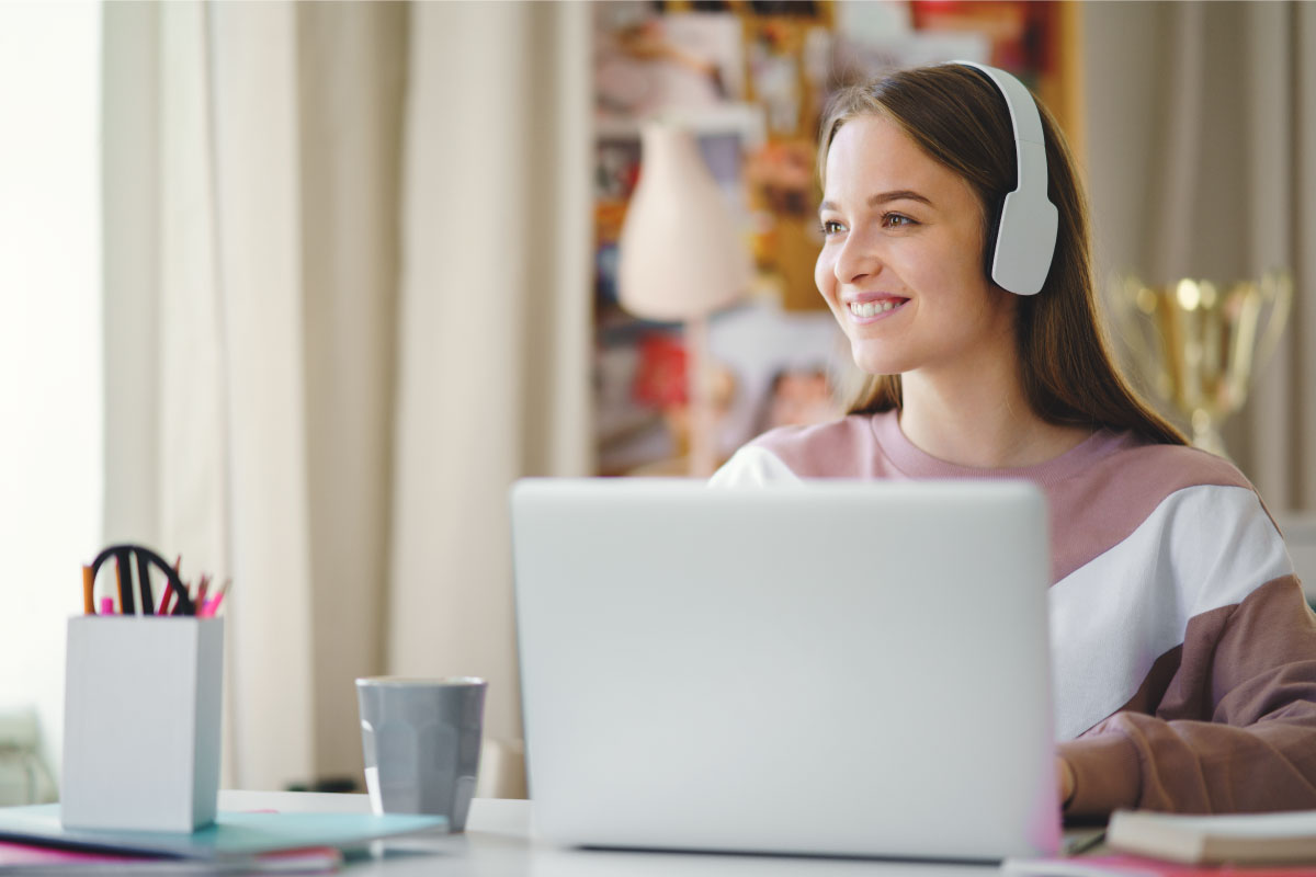 Mujer joven al frente de un computador y con audífonos