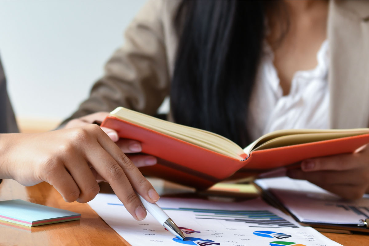 Una persona leyendo un libro y otra señalando un gráfico de torta