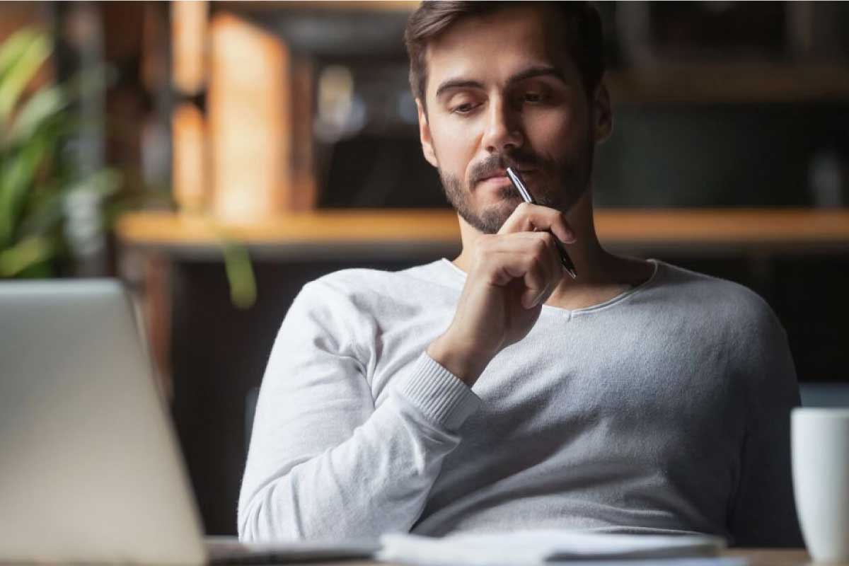 Hombre joven sentado, con un lapicero cerca a la boca y pensando.