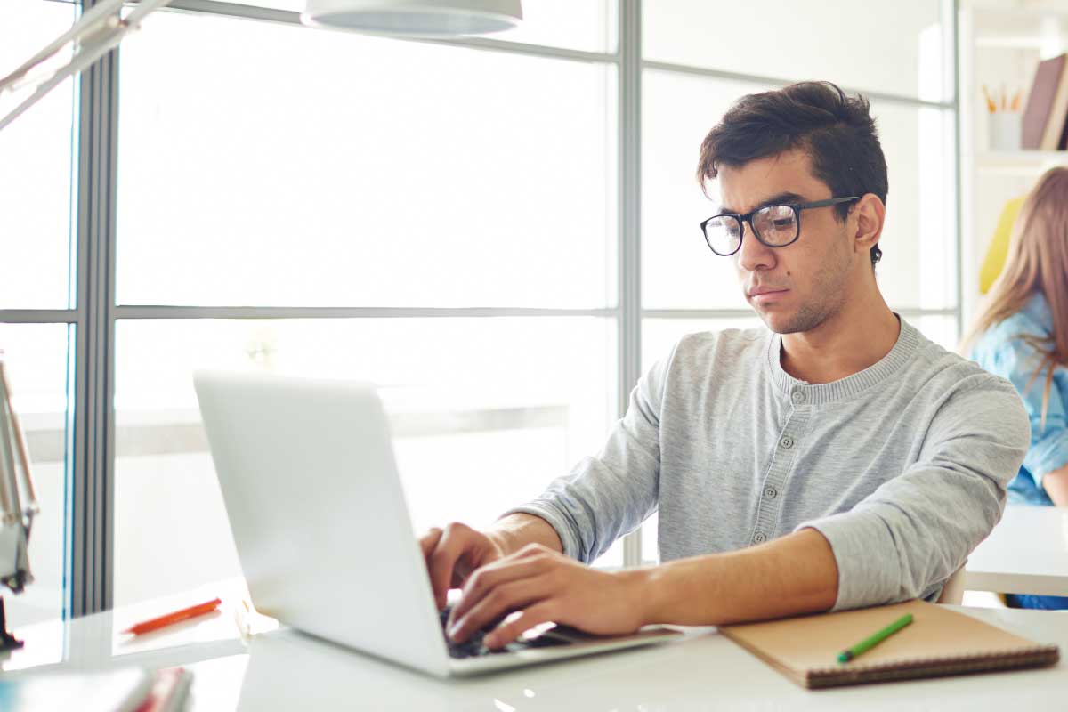 Joven escribiendo en un computador portatil.
