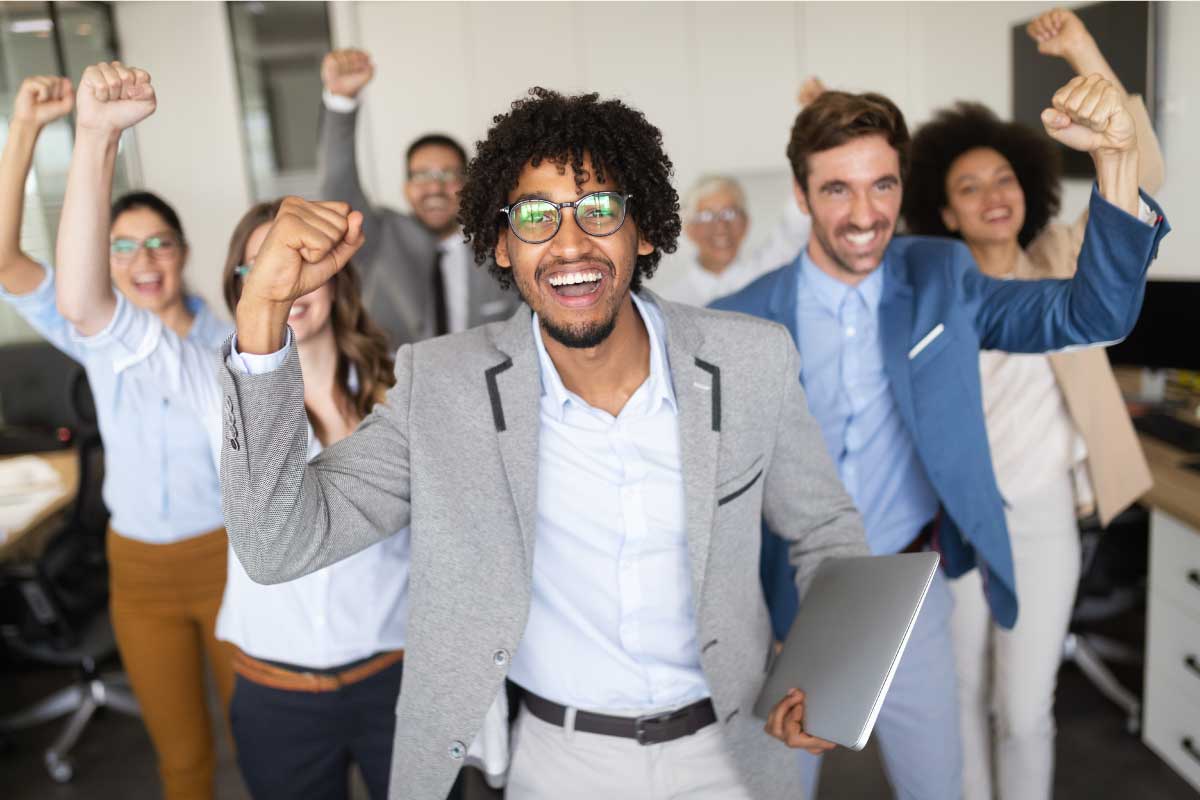 Grupo de jóvenes ejecutivos en la oficina celebrando alegremente con su mano empuñada y extendida hacia arriba.