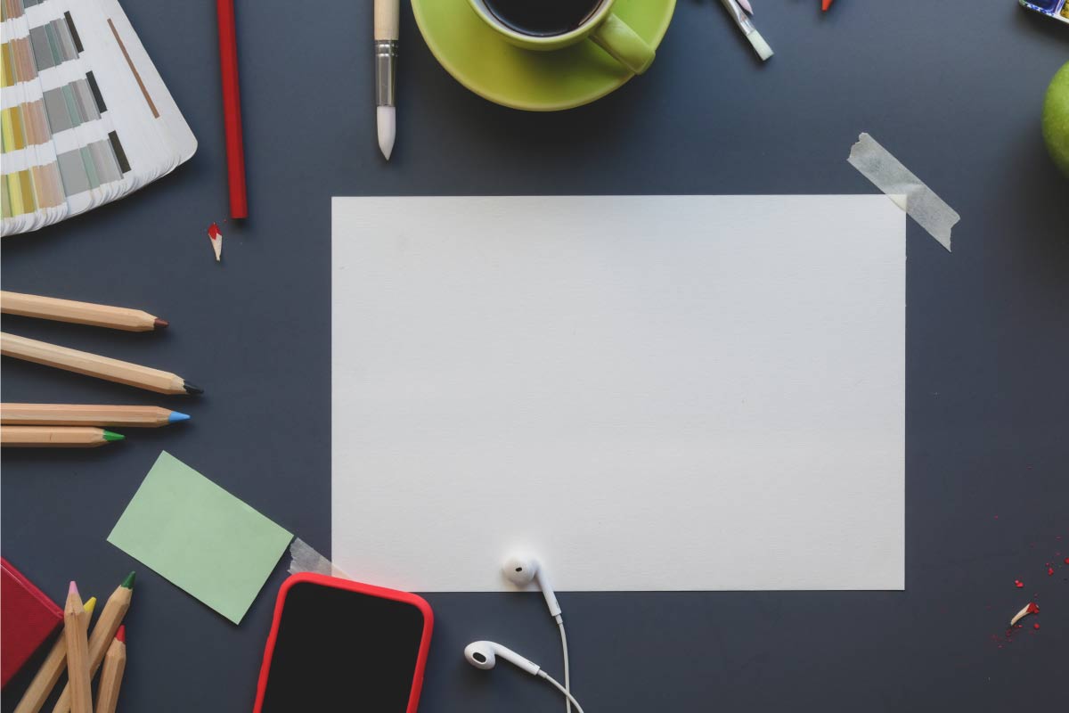 Toma superior de una mesa con una hoja de papel en blanco, lápices, lápices de colores, un café y un teléfono móvil.