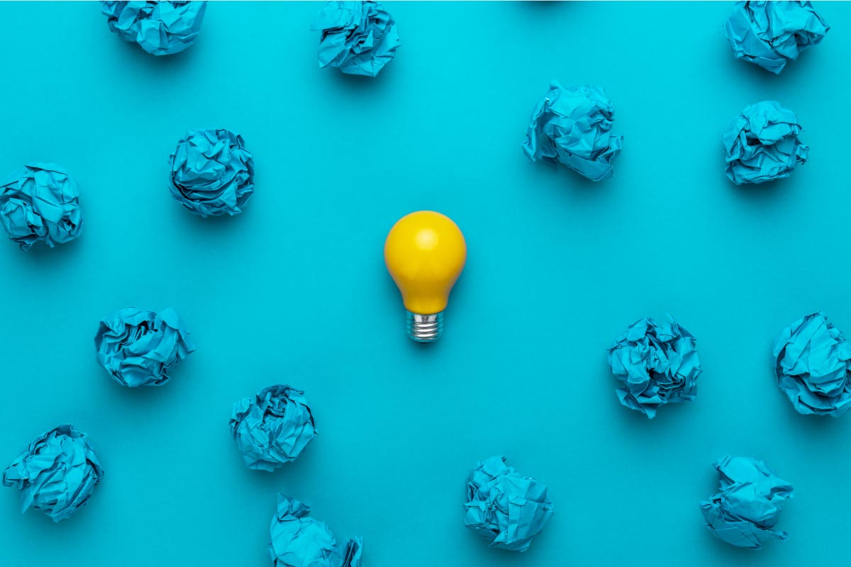 Bombilla amarilla en un fondo azul rodeada de bolas de papel azul arrugado