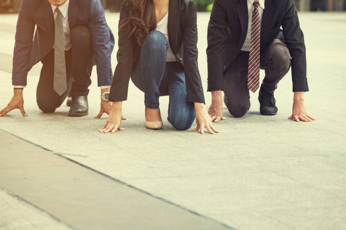 Tres ejecutivos en la calle, agachados con un rodilla y las manos en el suelo a punto de comenzar una carrera