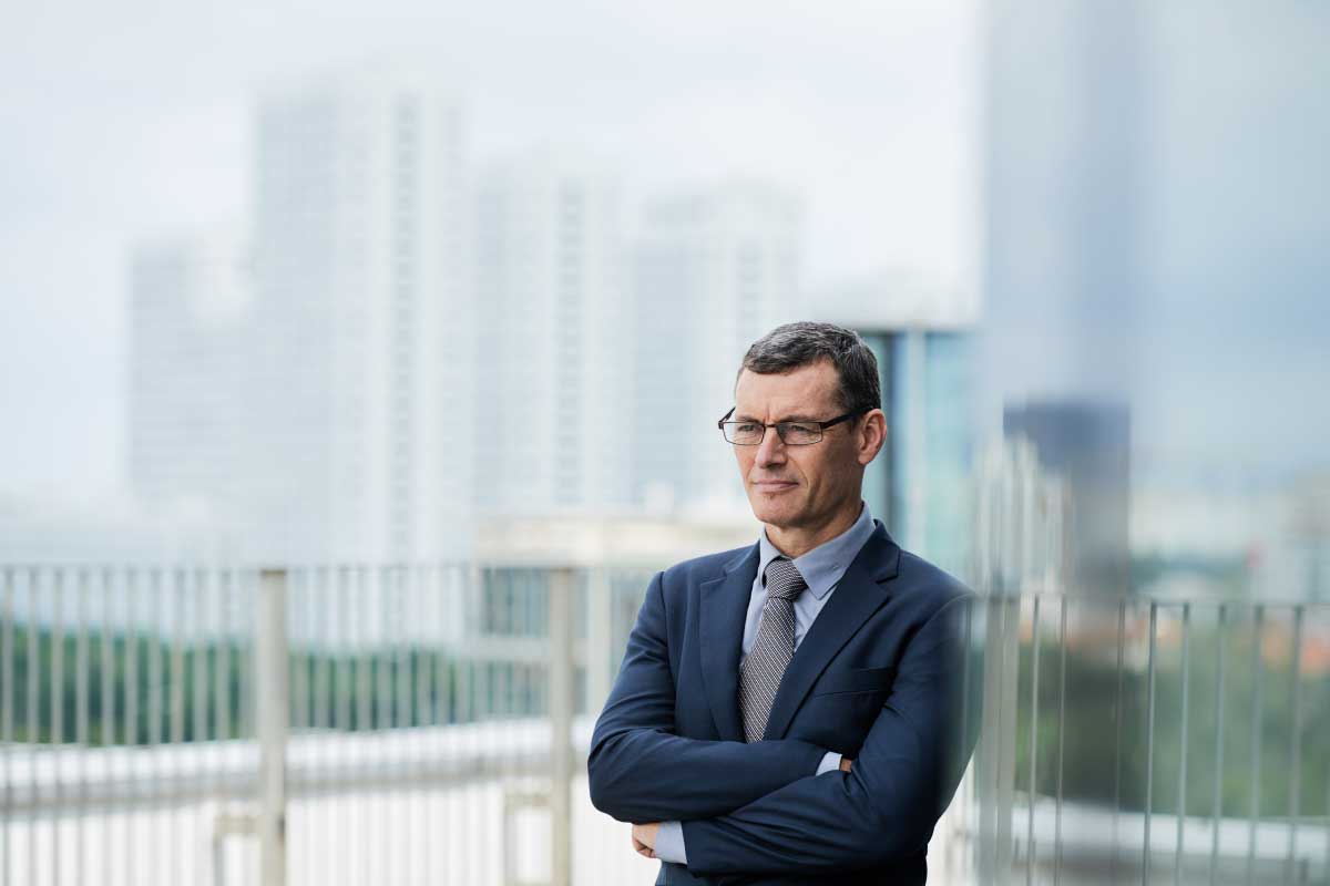 Hombre de negocios parado en una terraza de un edificio, con sus manos cruzadas y mirando a la distancia.