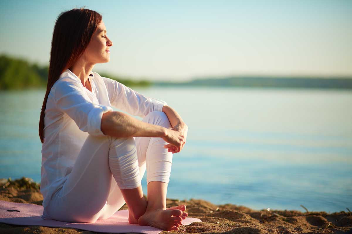 Mujer jovem sentada en la arena frente al mar con expresión de relajación