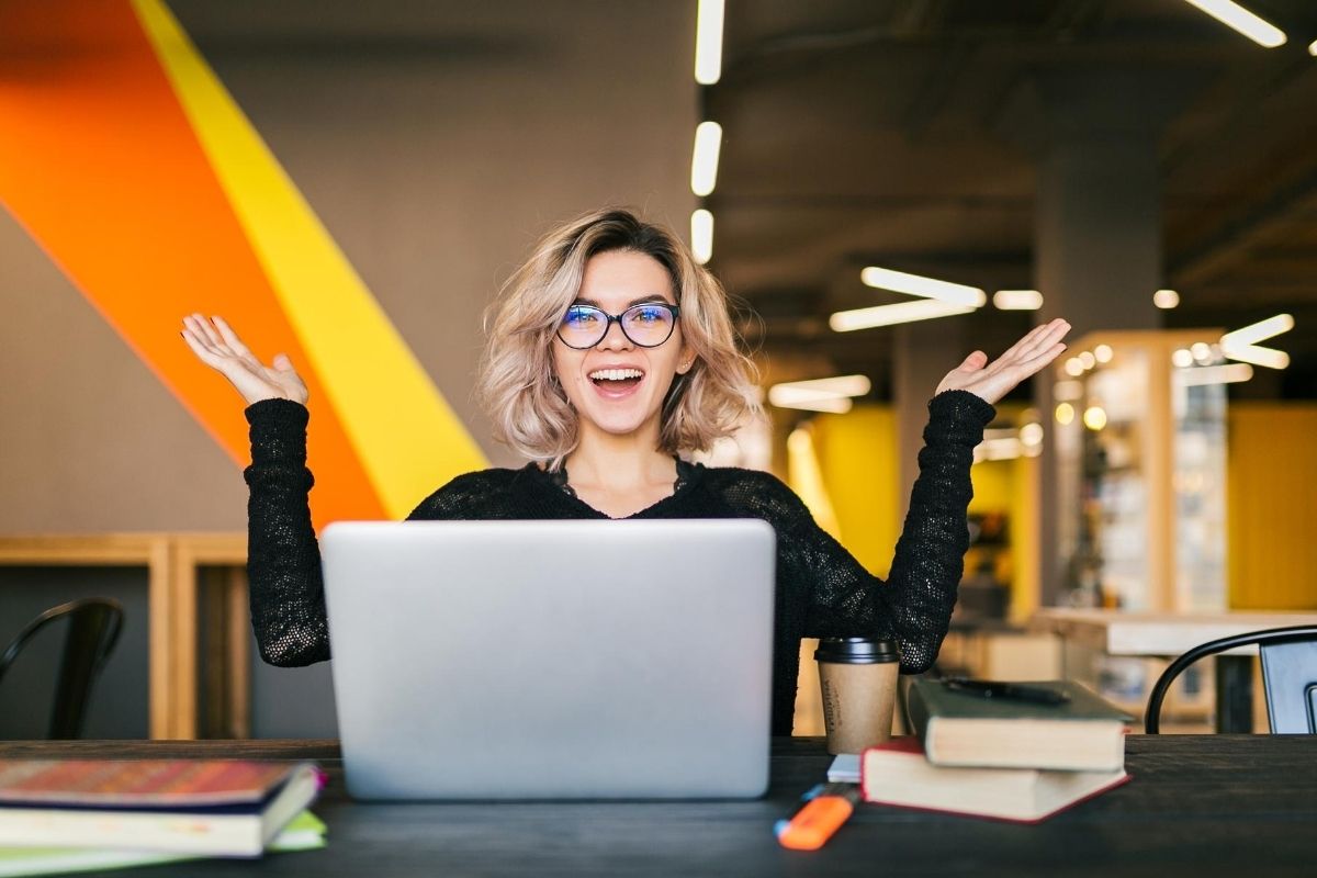 Mujer con los brazos abiertos y sonriendo al frente de un computador portatil