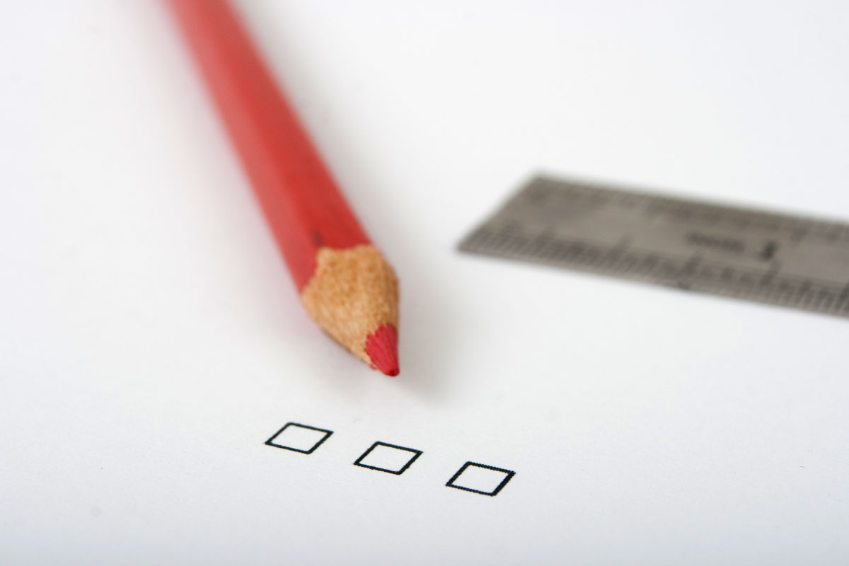 Acercamiento de un lápiz rojo cuya punta apunta a 3 cuadrados de contorno negro y una regla en el fondo.