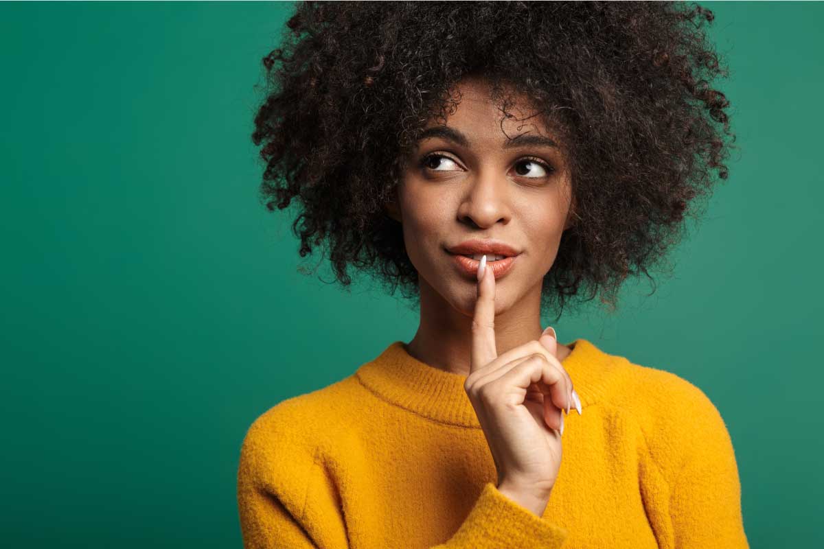 Mujer joven con el dedo índice sobre sus labios, mirando hacia el un lado, pensando.