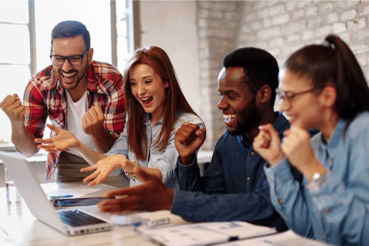 Cuatro personas jóvenes mirando un computador portatil y celebrando.
