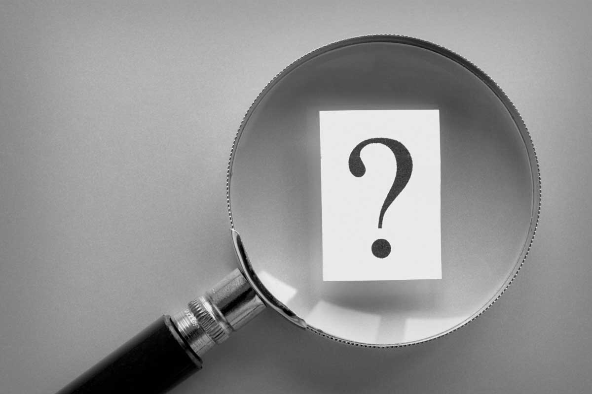 Acercamiento de una lupa la cual está aumentando un signo de interrogación.