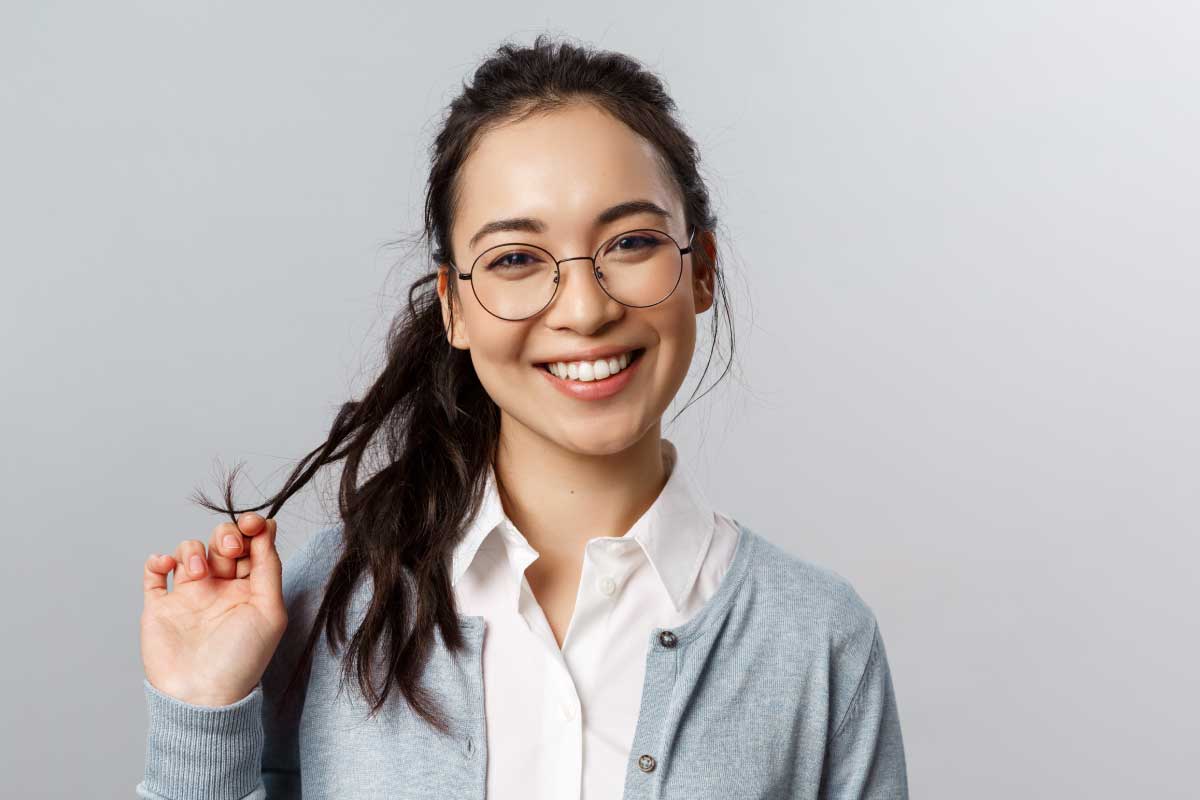 Mujer joven mirando sonriente a la cámara, cogiendo una hebra de su pelo.