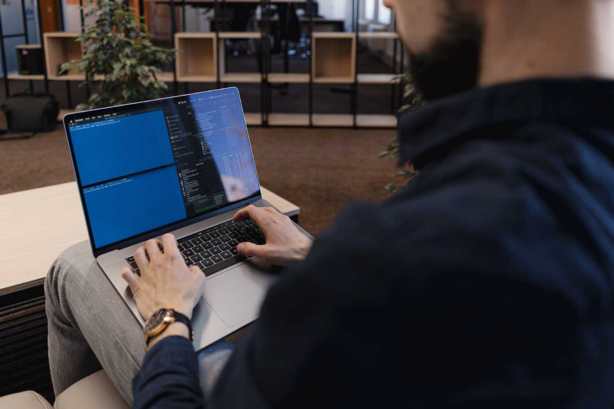 Hombre joven sentado con un computador portatil en sus piernas, trabajando en él.