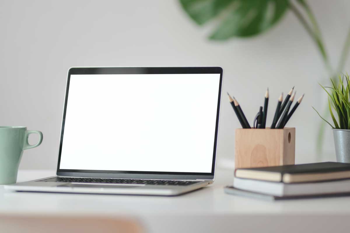 Toma de un escritorio con computador portatil abierto, un pocillo, unas libretas y unos lápices en un recipiente.