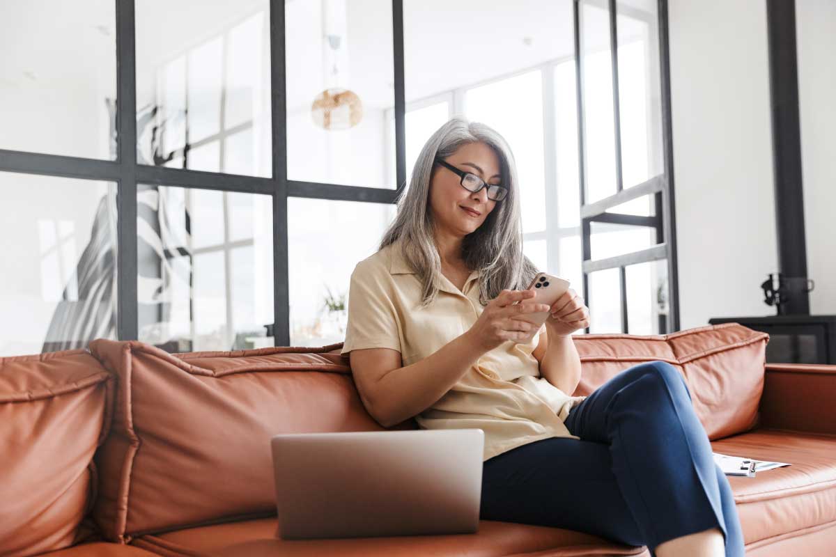 Mujer de negocios sentada en un sofá revisando un teléfono móvil.