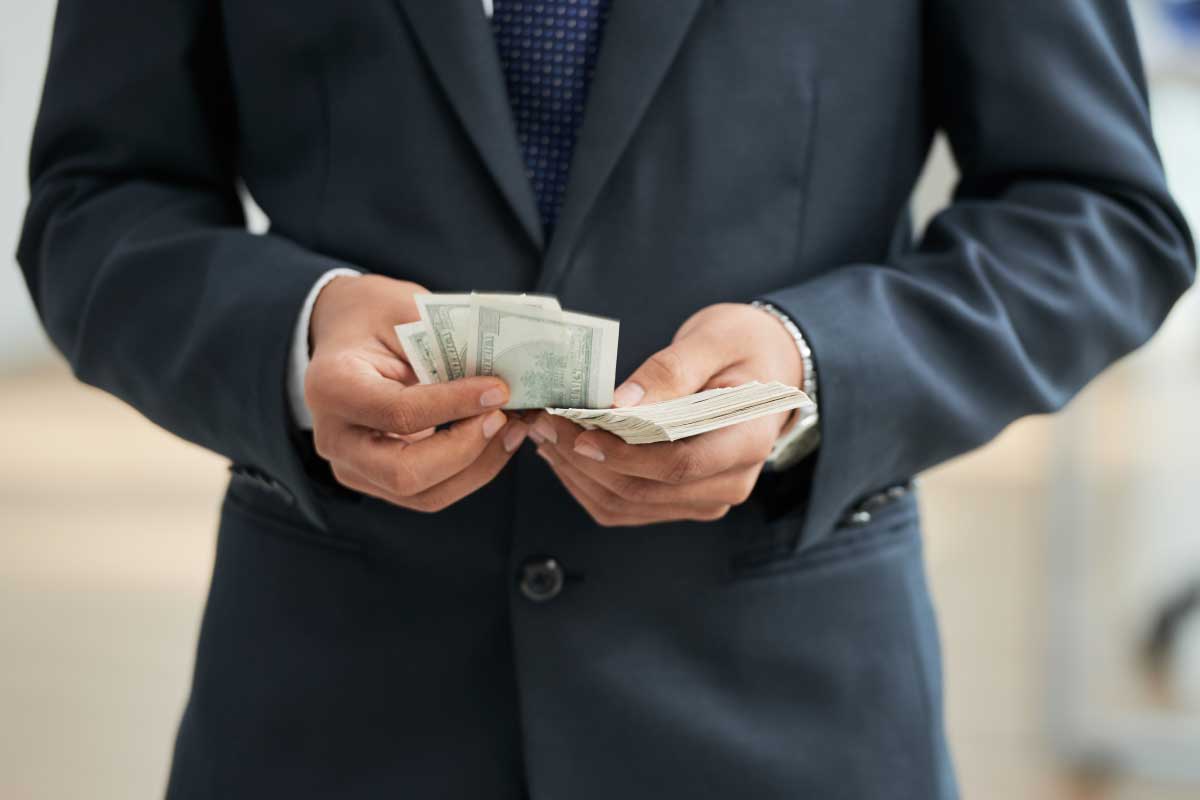 Acercamiento de torso de un hombre de negocios, sosteniendo y contando billetes.