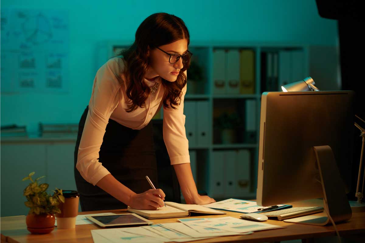 Mujer joven tomando notas al frente de un computador.