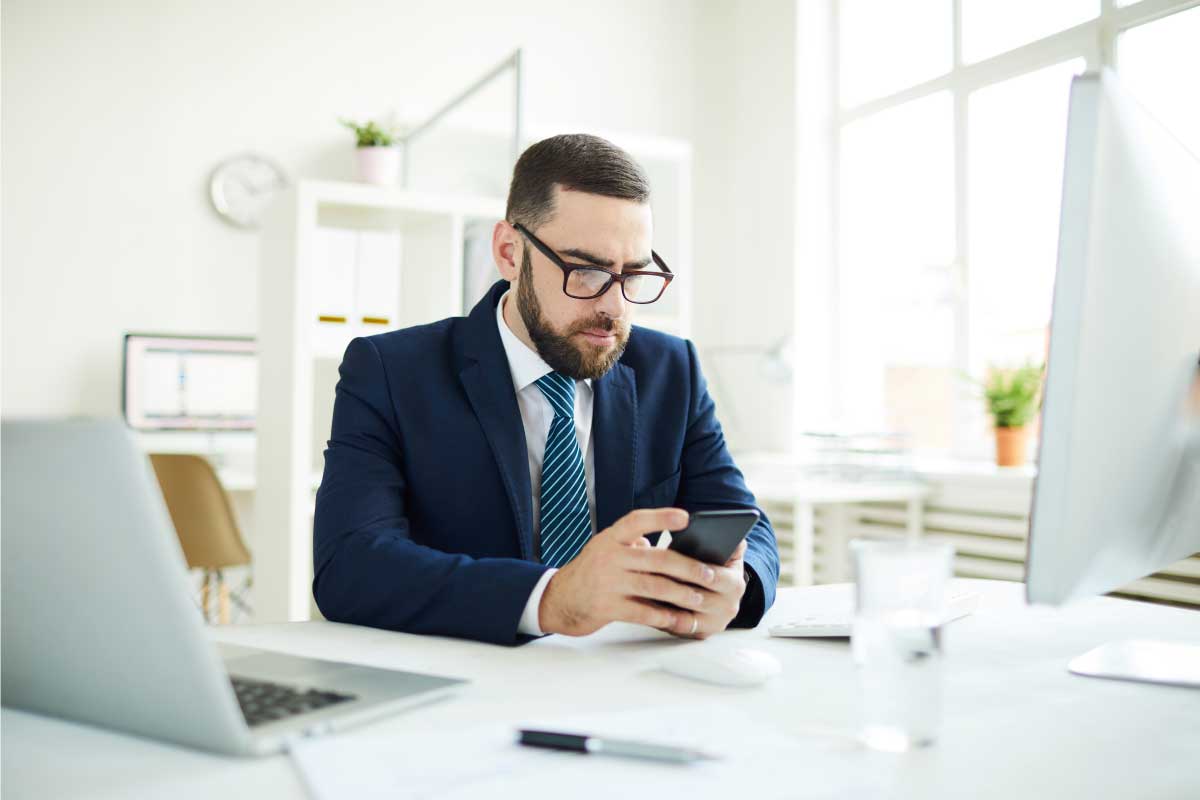 Hombre ejecutivo sentado al frente de un escritorio mirando un teléfono inteligente.