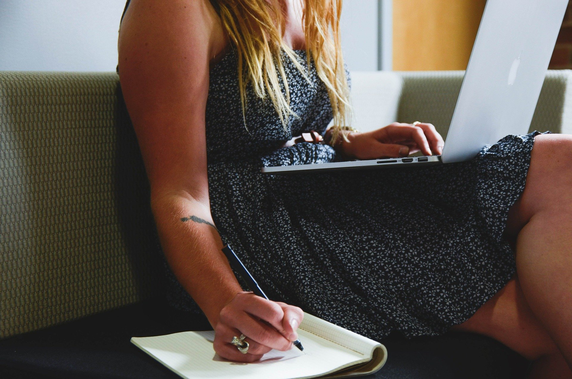 Mujer sentada con un computador portatil y escribiendo en un cuaderno