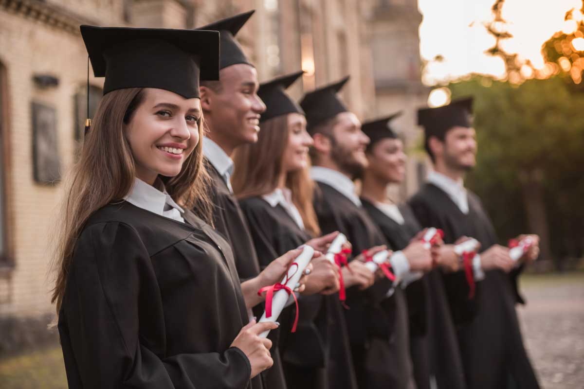 Grupo de jóvenes graduados vistiendo toga y birrete, sosteniendo su diploma.