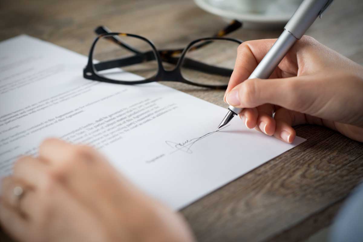 Toma cercana de las manos de una persona firmando un documento con una pluma fuente.
