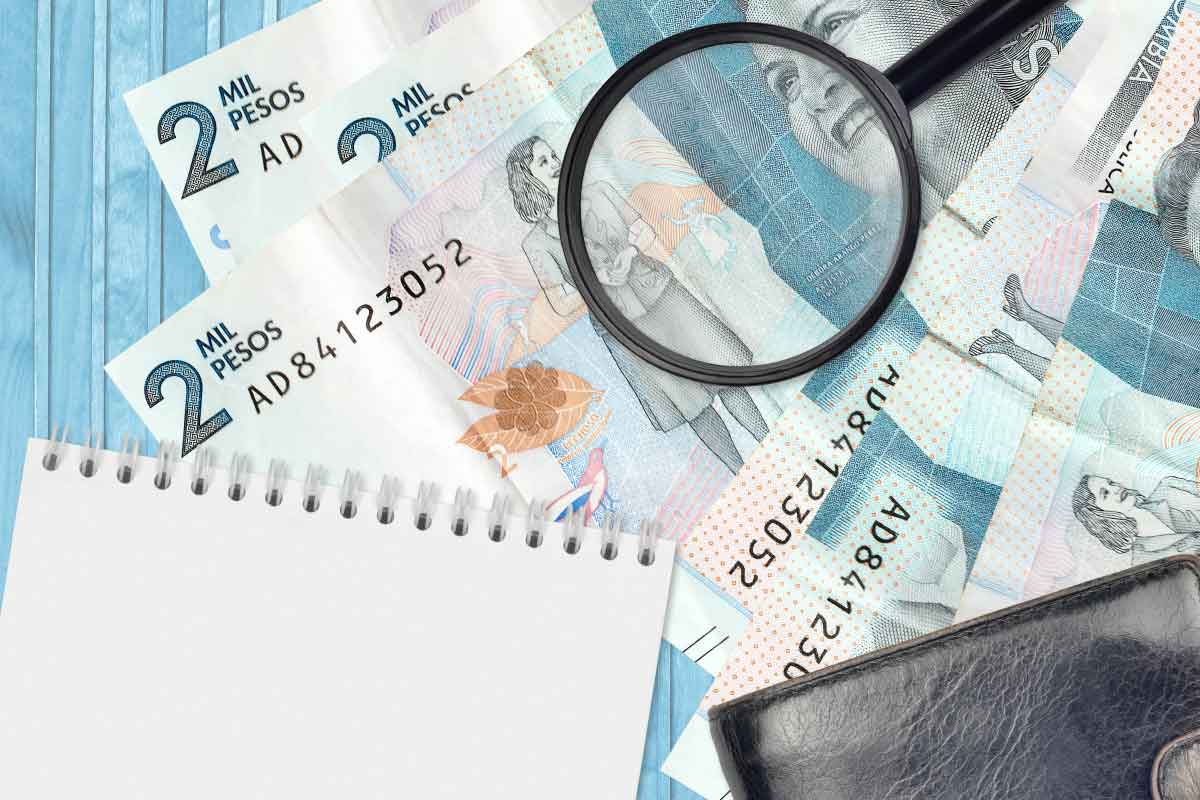 Acercamiento de varios billetes sobre los que hay una lupa, una libreta y una billetera