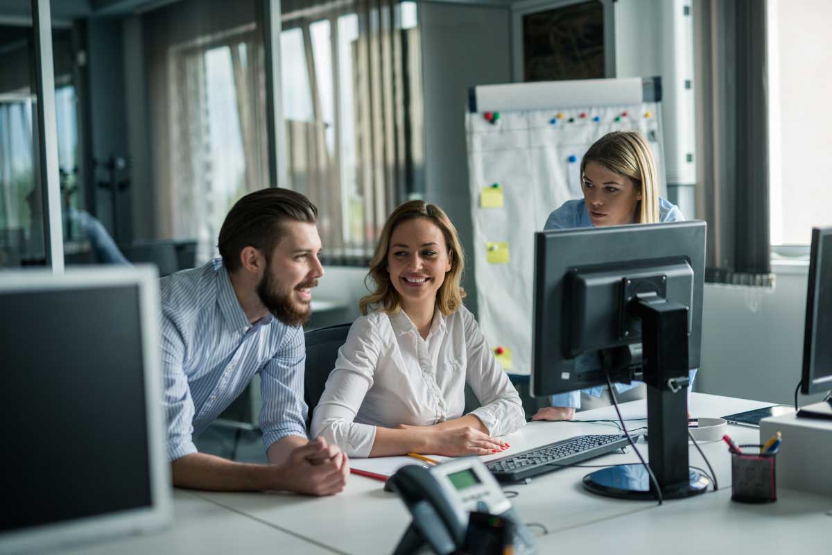 Tres personas jóvenes en un oficina, mirando la pantalla de un computador.