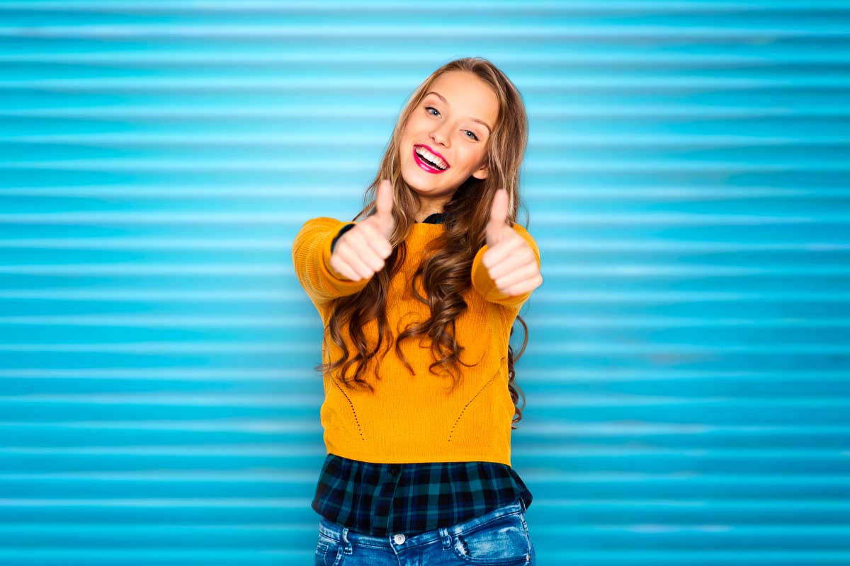 Mujer joven mirando a la cámara con los pulgares arriba y sonriendo.