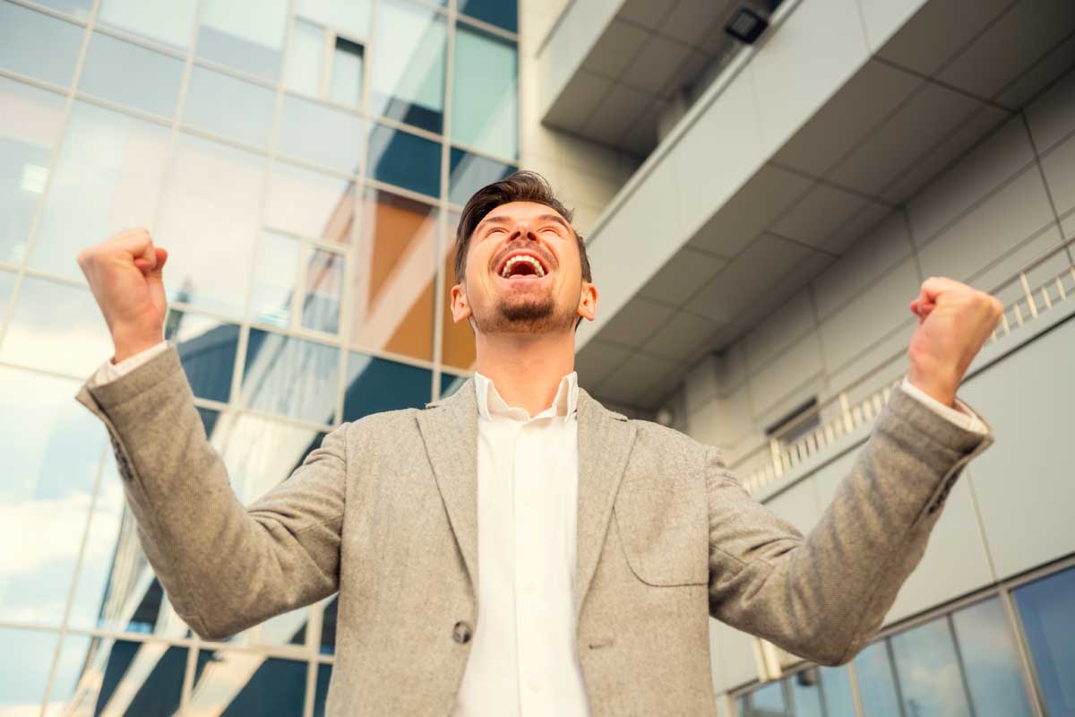Hombre joven con las manos empuñadas hacia arriba y sonriendo.