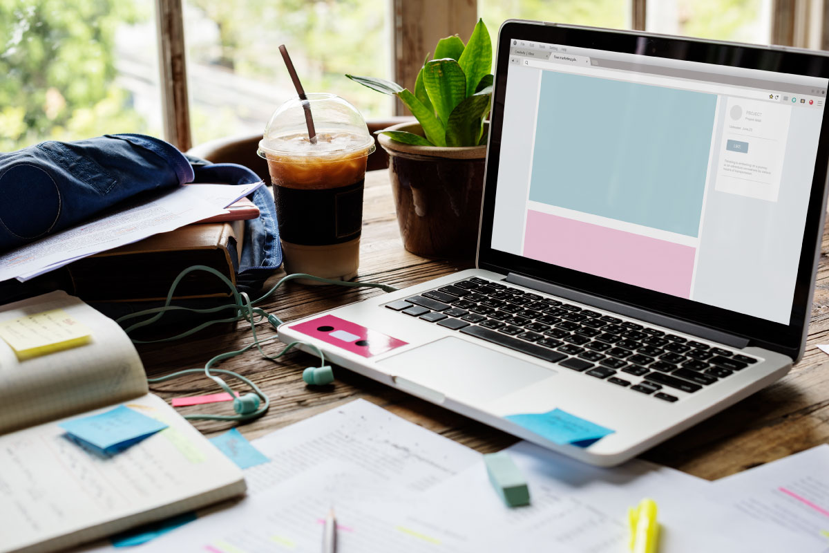 Escritorio con un computador portatil, una libreta, papeles con notas y varios elementos de oficiana.