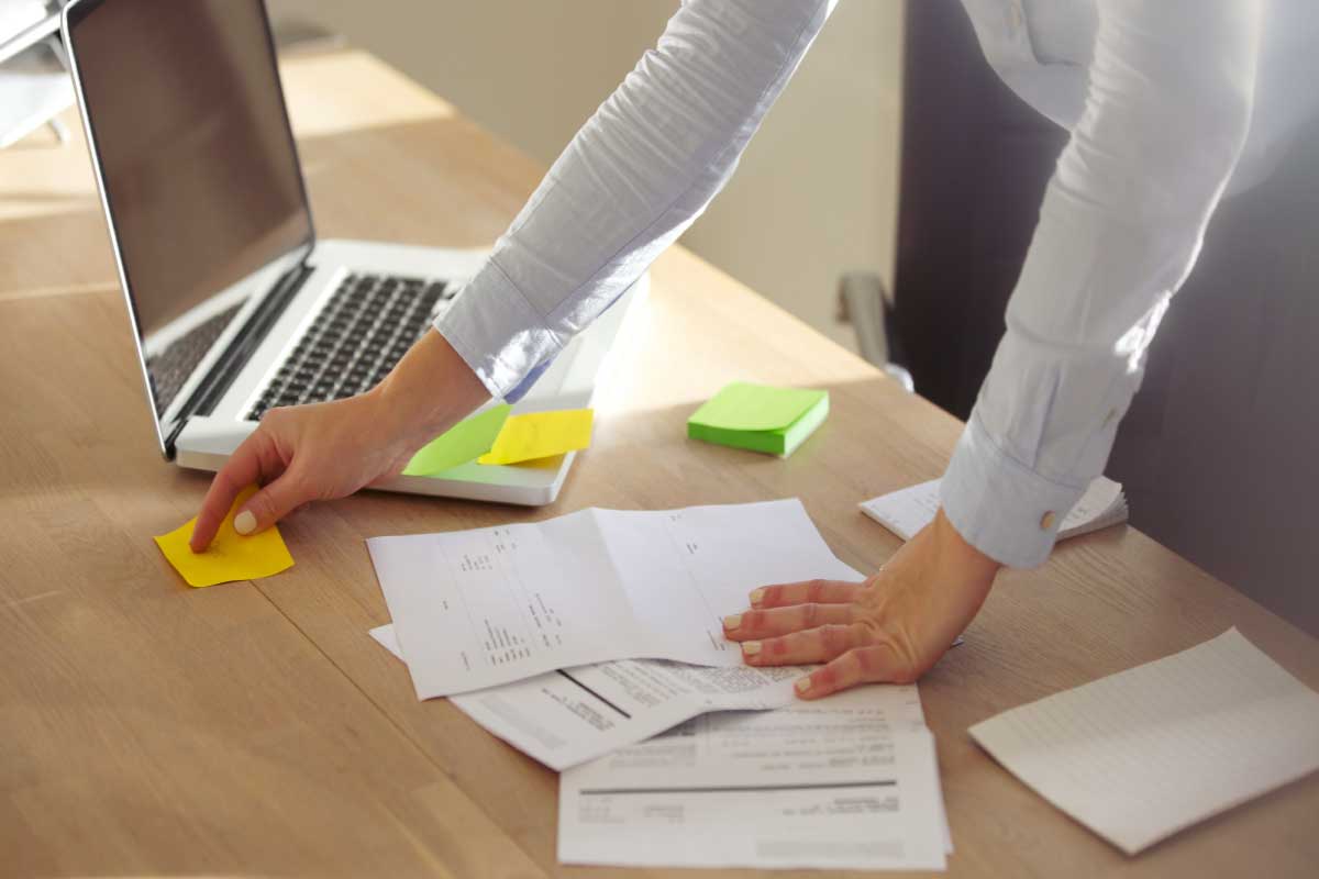Persona parada frente a su computador con hojas de papel