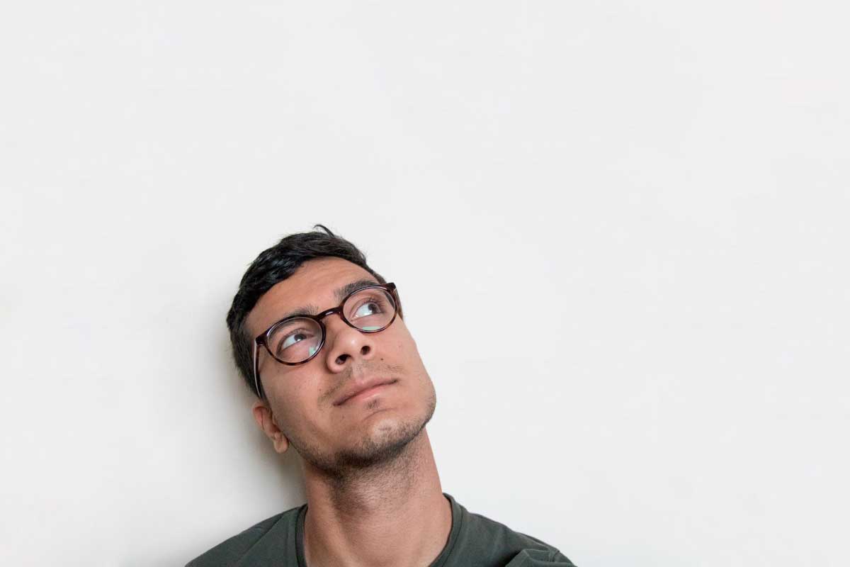 Hombre joven con lentes, mirando hacia arriba y pensando.