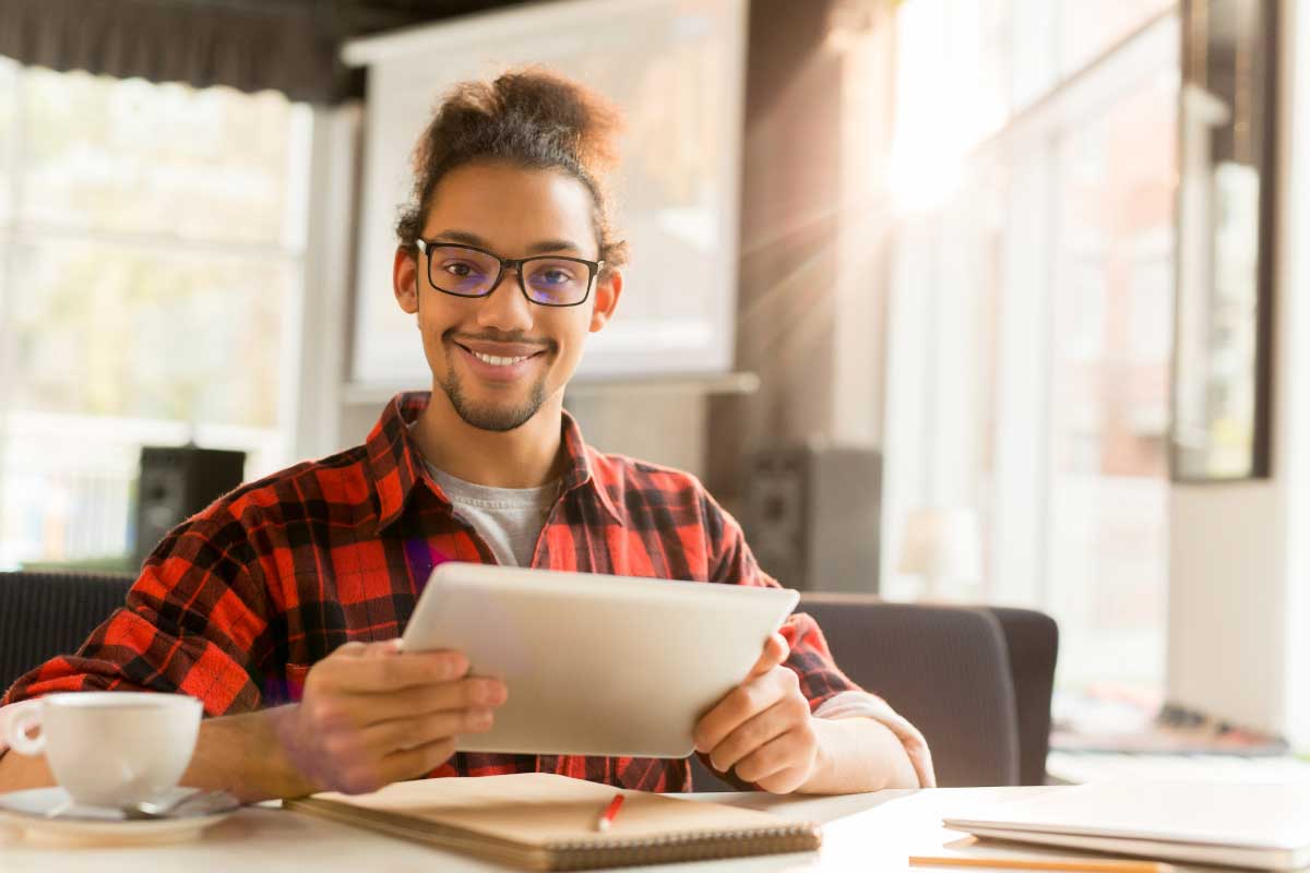 Hombre joven, sonriendo hacia la cámara, con una tableta en sus manos.