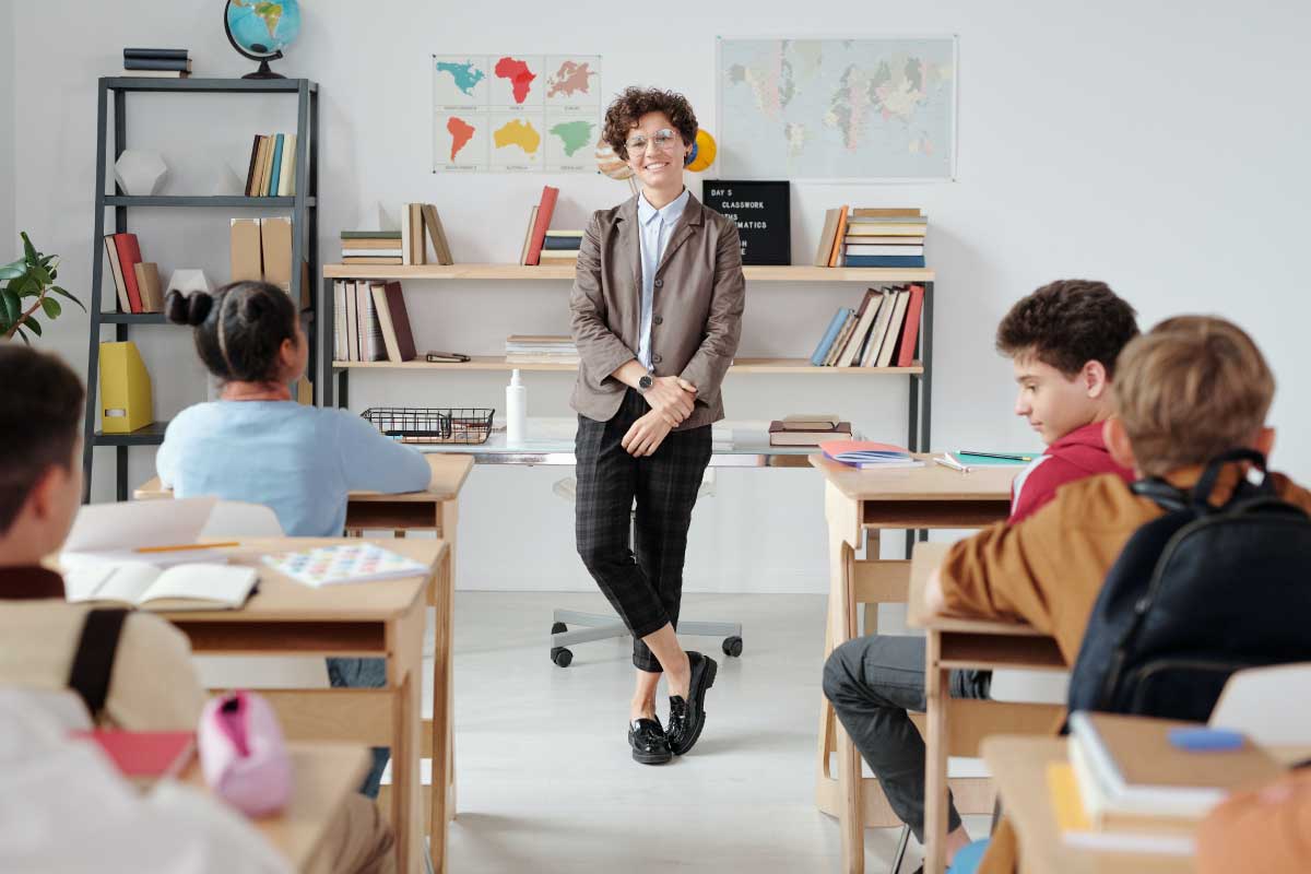 Profesora parada al frente de un salón de clase de niños atentamente mirándola