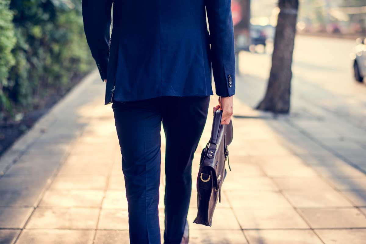 Vista trasera un hombre caminado en la calle, sosteniendo un maletín ejecutivo o portadocumentos.