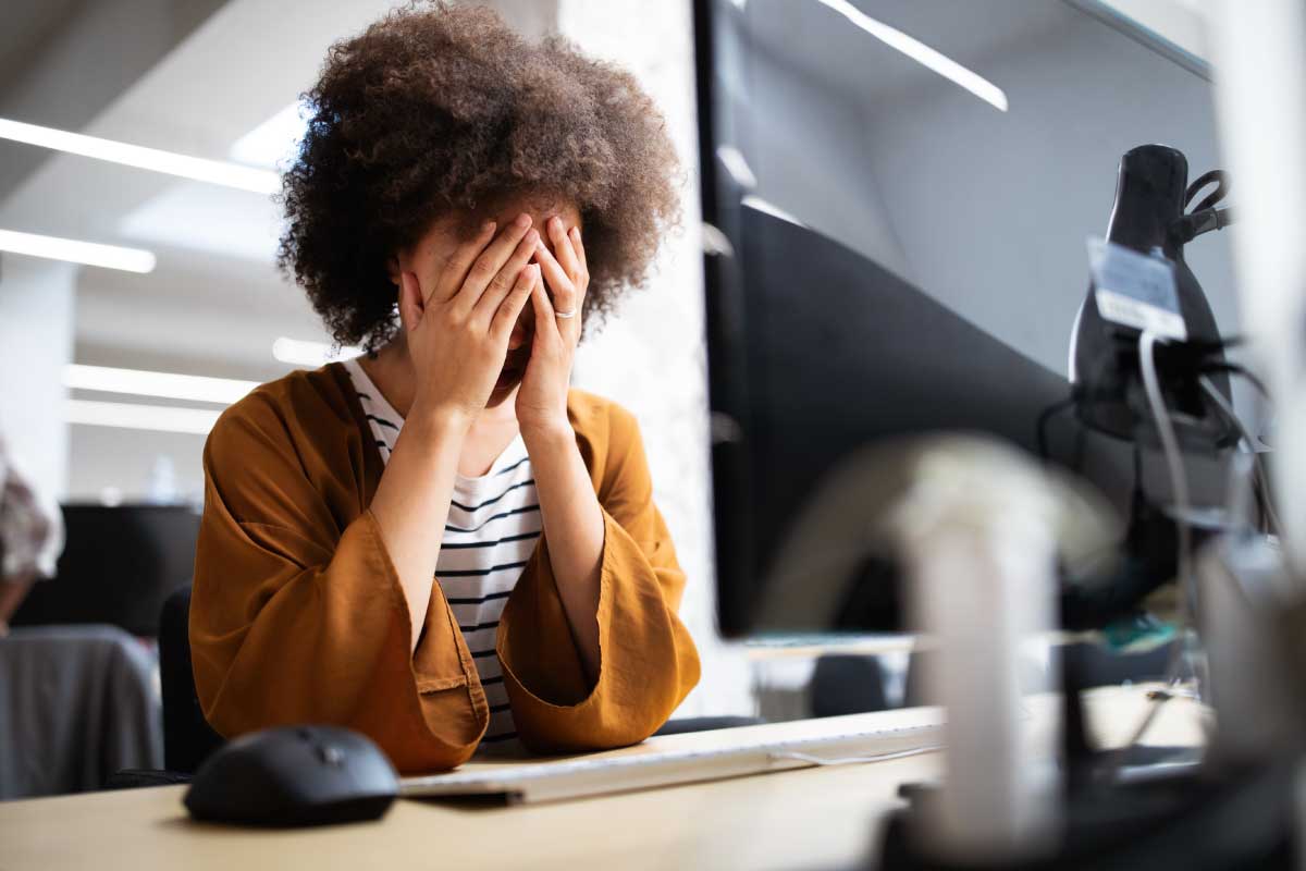 Mujer sentada al frente de un escritorio con las manos sobre su cara.