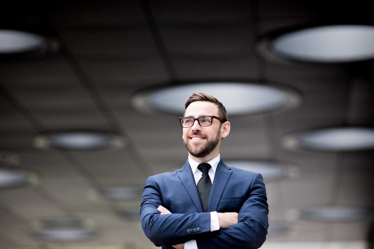 Hombre de negocios joven parado con las manos cruzadas mirando hacia la izquierda