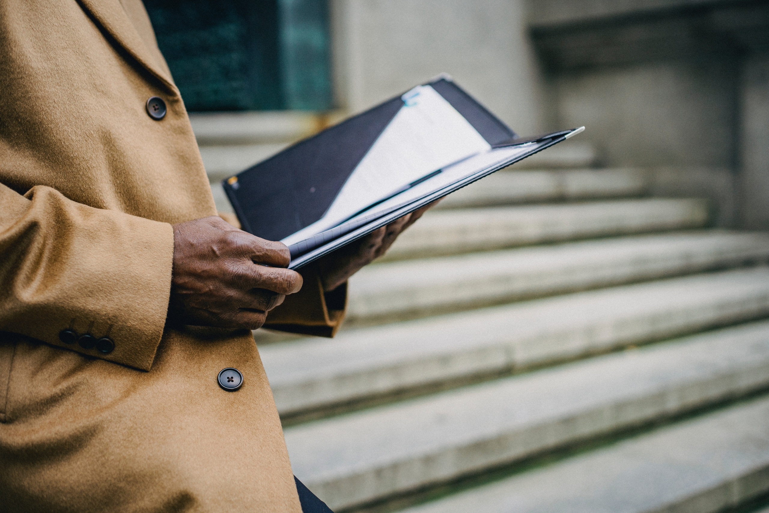 Hombre bajando una escalas en exteriores sosteniendo una carpeta abierta con documentos.