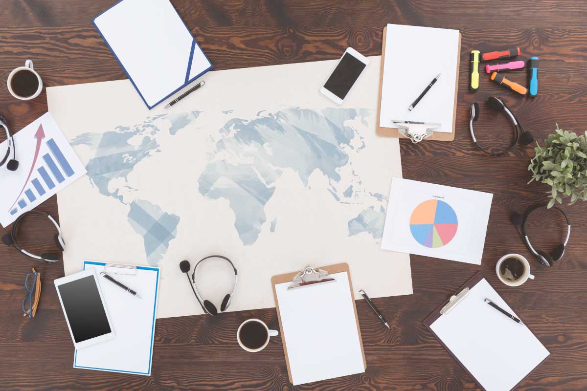 Vista superior de una mesa con cuadernos, audífonos, lápices, marcadores, un mapa del mundo en papel.