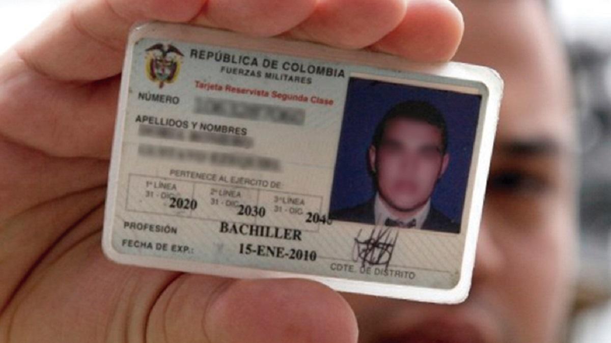 Hombre sosteniendo al frente de su cara el carnet de su libreta militar en donde los nombres y fotografía están borrosos.